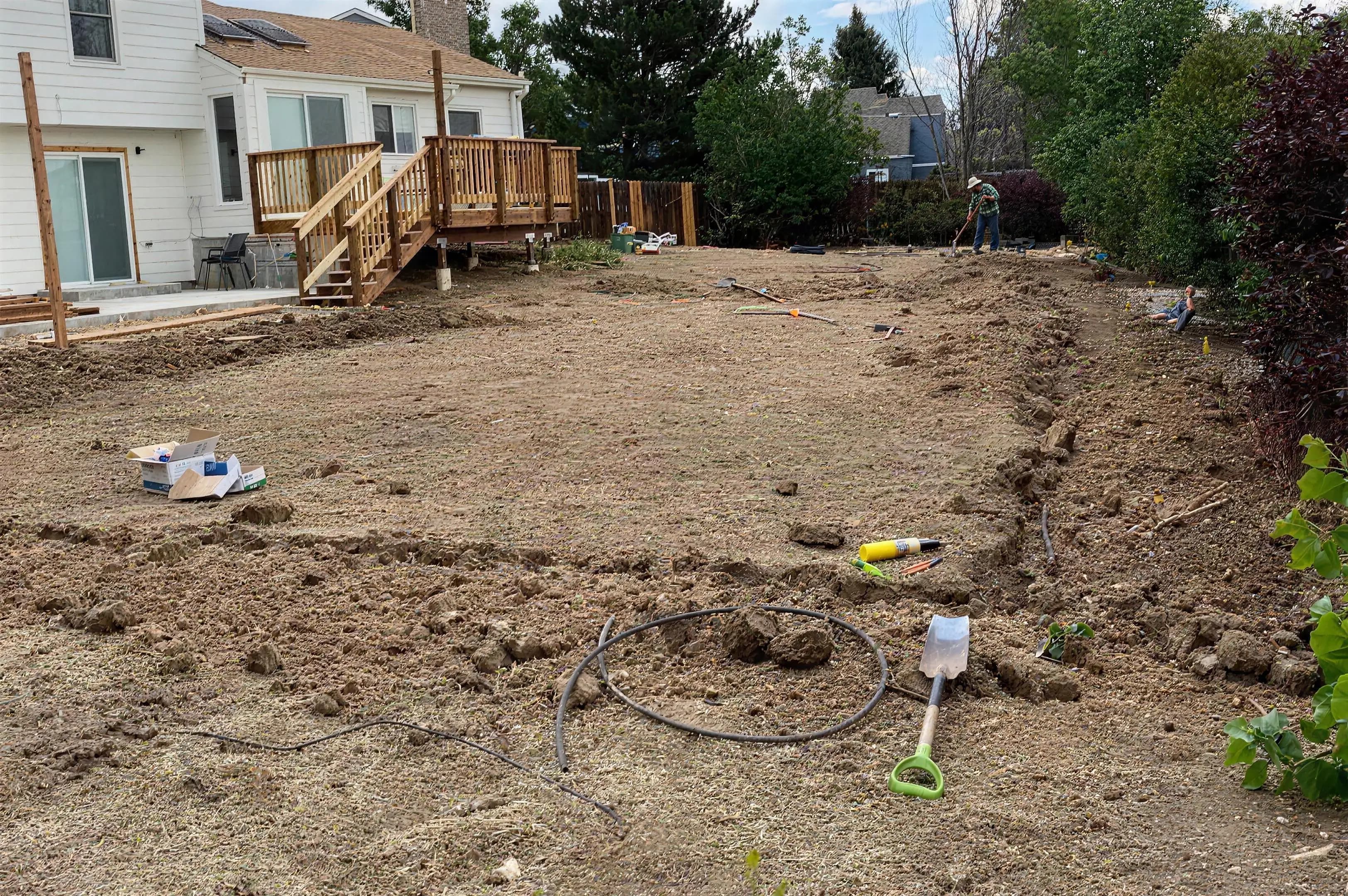 Backyard graded to bare soil with irrigation lines being trenched before a new lawn