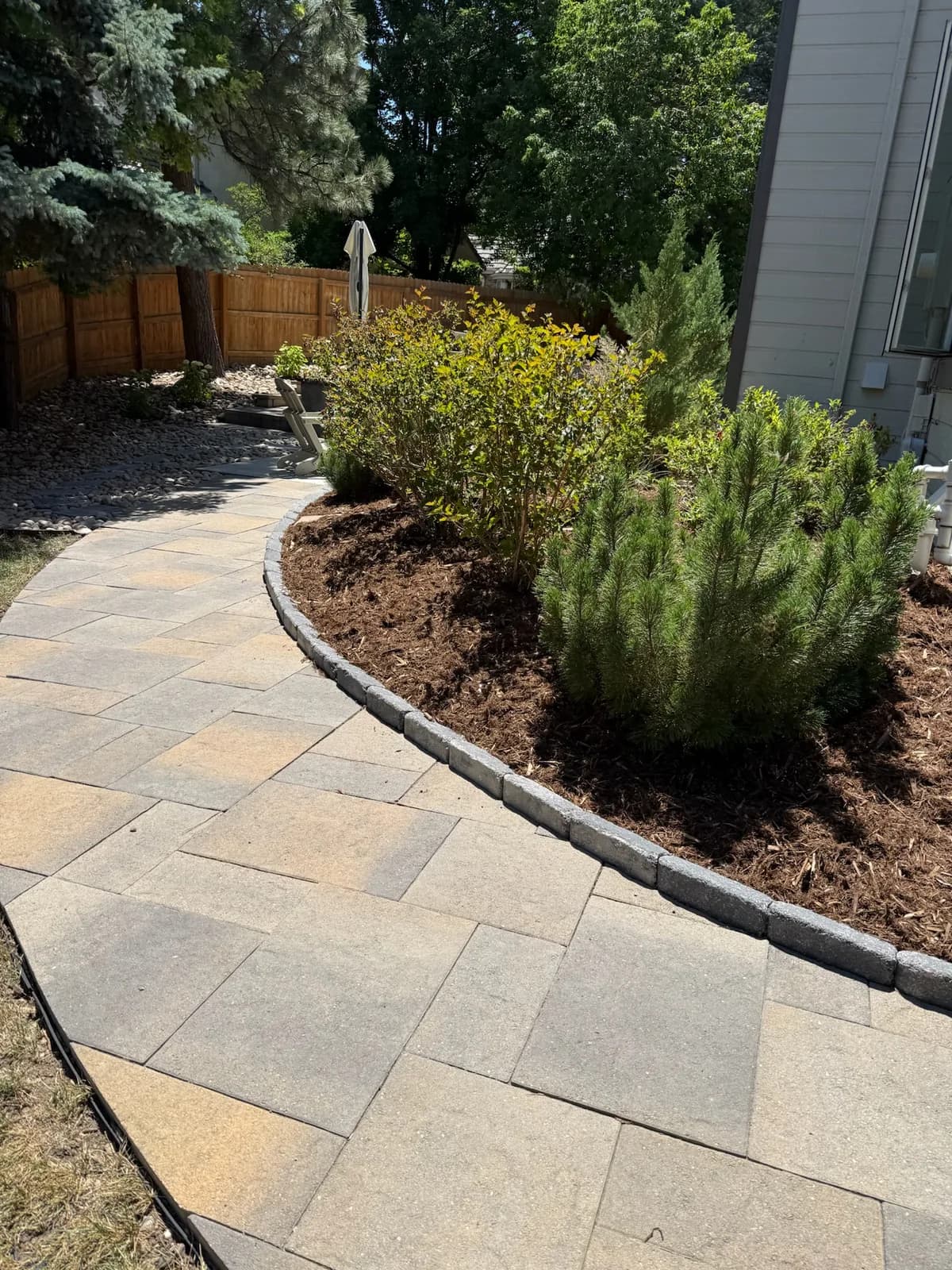 Flagstone walkway curving past a water-wise bed of evergreens and boulders