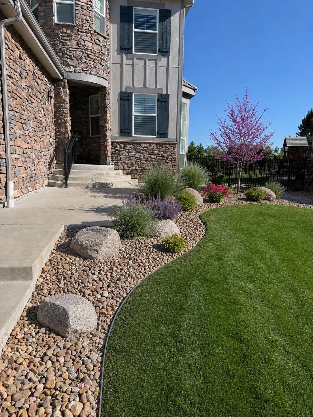 Front-yard rock bed with ornamental grasses beside a curved, freshly mowed lawn edge