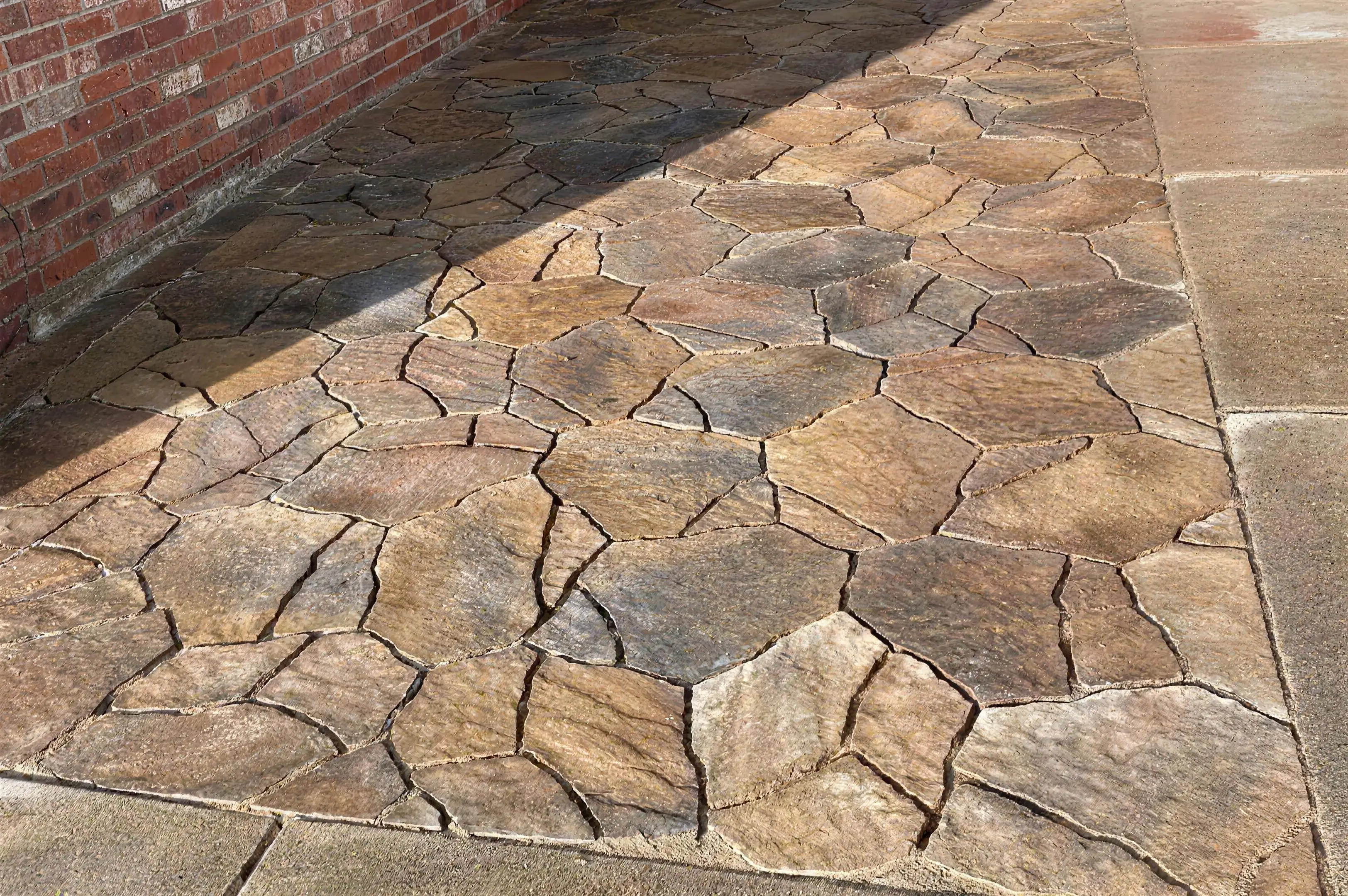 Flagstone-style paver walkway laid alongside a brick wall
