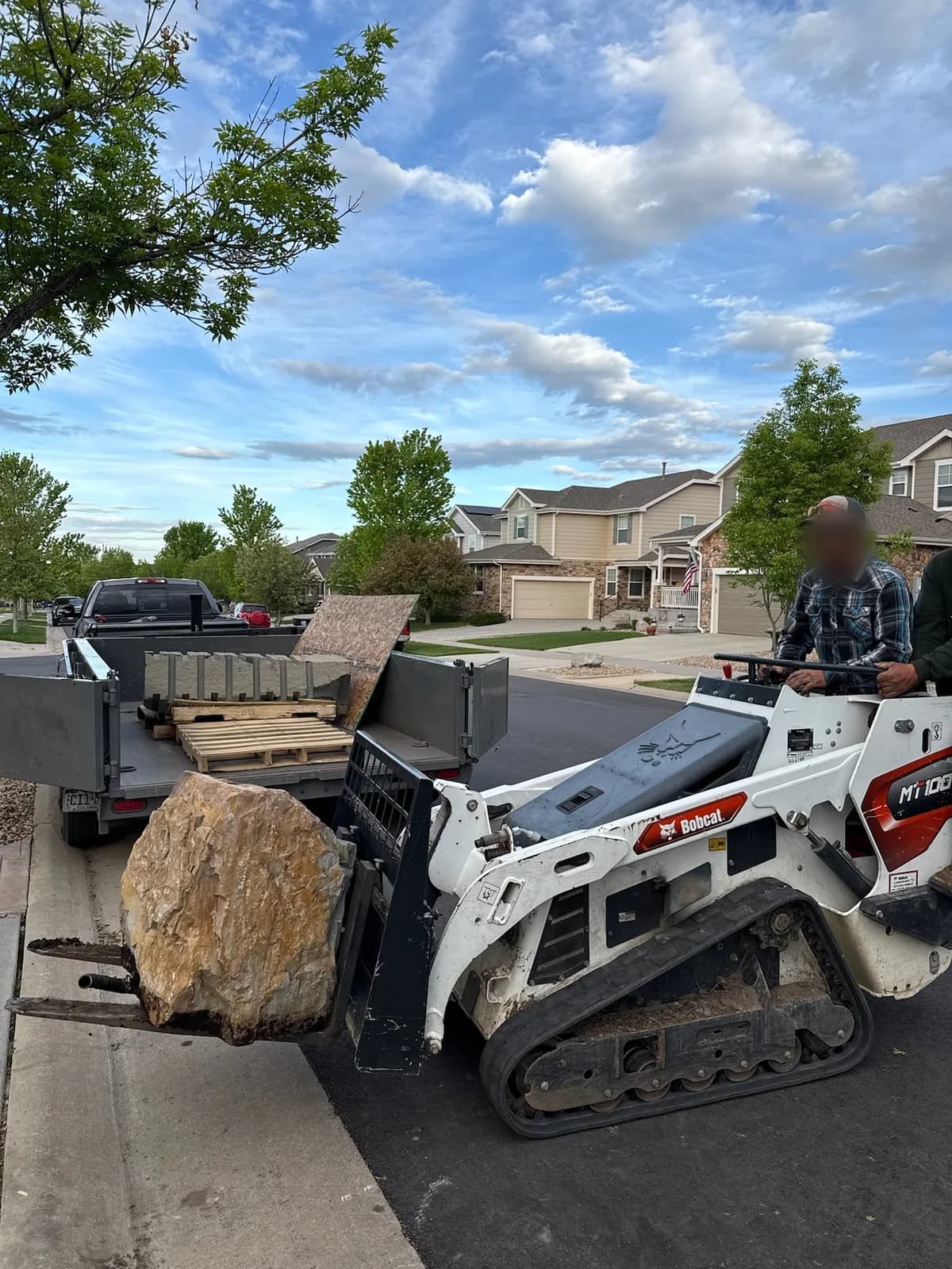 A T&T crew member placing a large boulder with a compact track loader