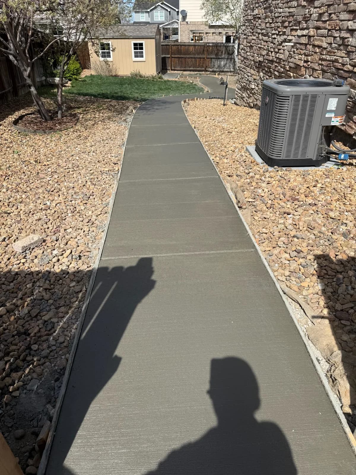 Wide concrete walkway running between rock beds along the side of a home