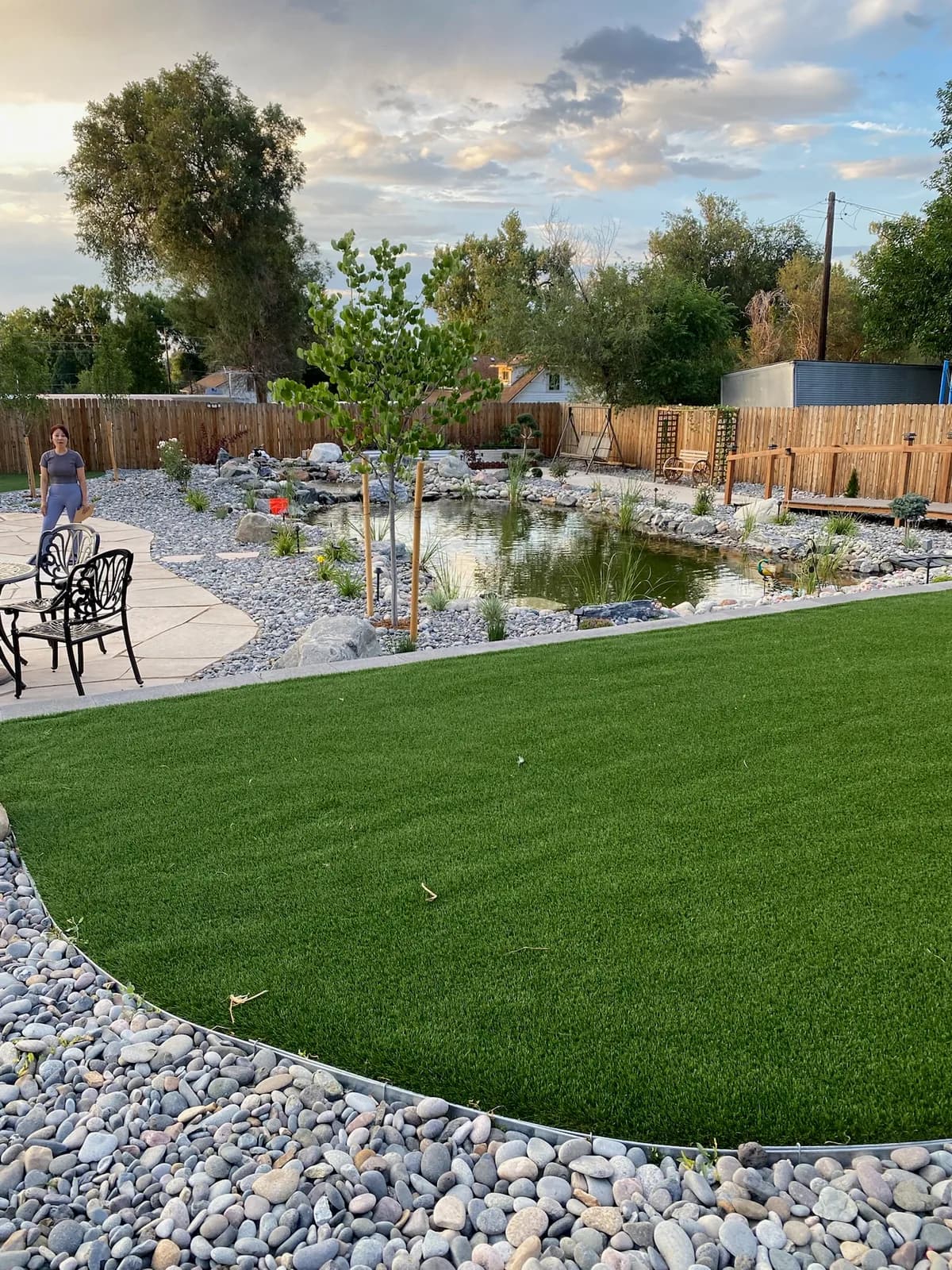 Wide backyard with a manicured lawn, patio seating, and a pond beyond